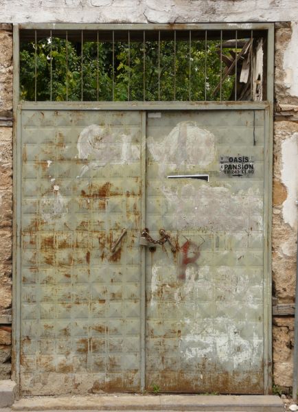 Grey metal door with grid pattern and lock and chain. Surface has rust and paint spots.